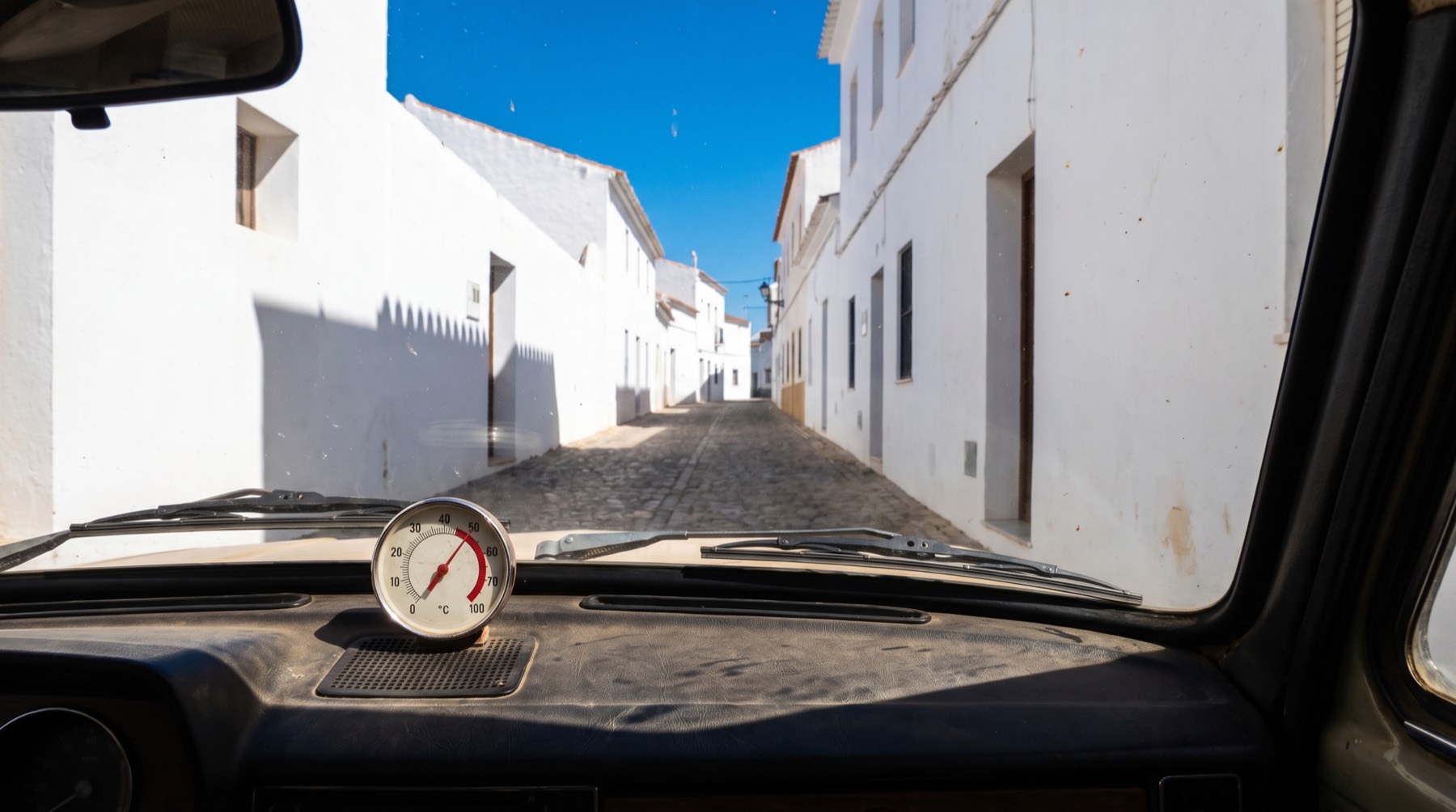 Salpicadero de un coche aparcado al sol del mediodía en una calle mediterránea encalada